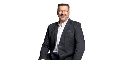 Der Mann trägt eine Brille und hat einen gepflegten Bart, während er freundlich in die Kamera schaut.