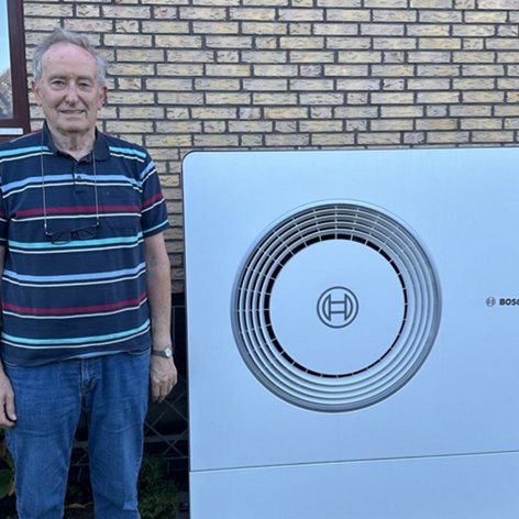 Ein freundlicher älterer Herr posiert neben einer Bosch-Klimaanlage, die in einem gepflegten Garten installiert ist.