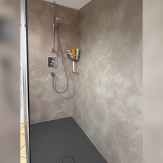 Die Dusche zeigt eine praktische Anordnung mit einem Handbrausekopf und einem Regal, das verschiedene Pflegeprodukte hält.