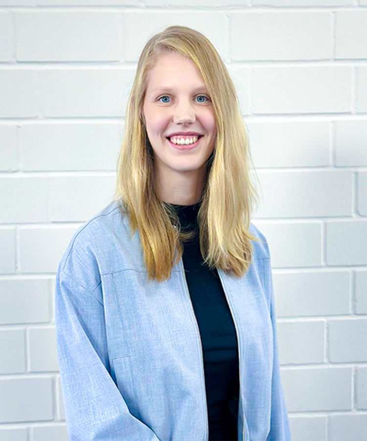 Die junge Frau hat eine entspannte Haltung und zeigt ihre Zähne in einem herzlichen Lächeln vor einer neutralen Kulisse.