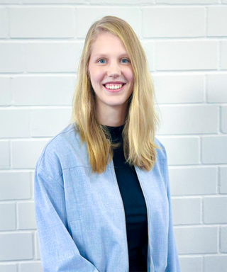 Die junge Frau hat eine entspannte Haltung und zeigt ihre Zähne in einem herzlichen Lächeln vor einer neutralen Kulisse.