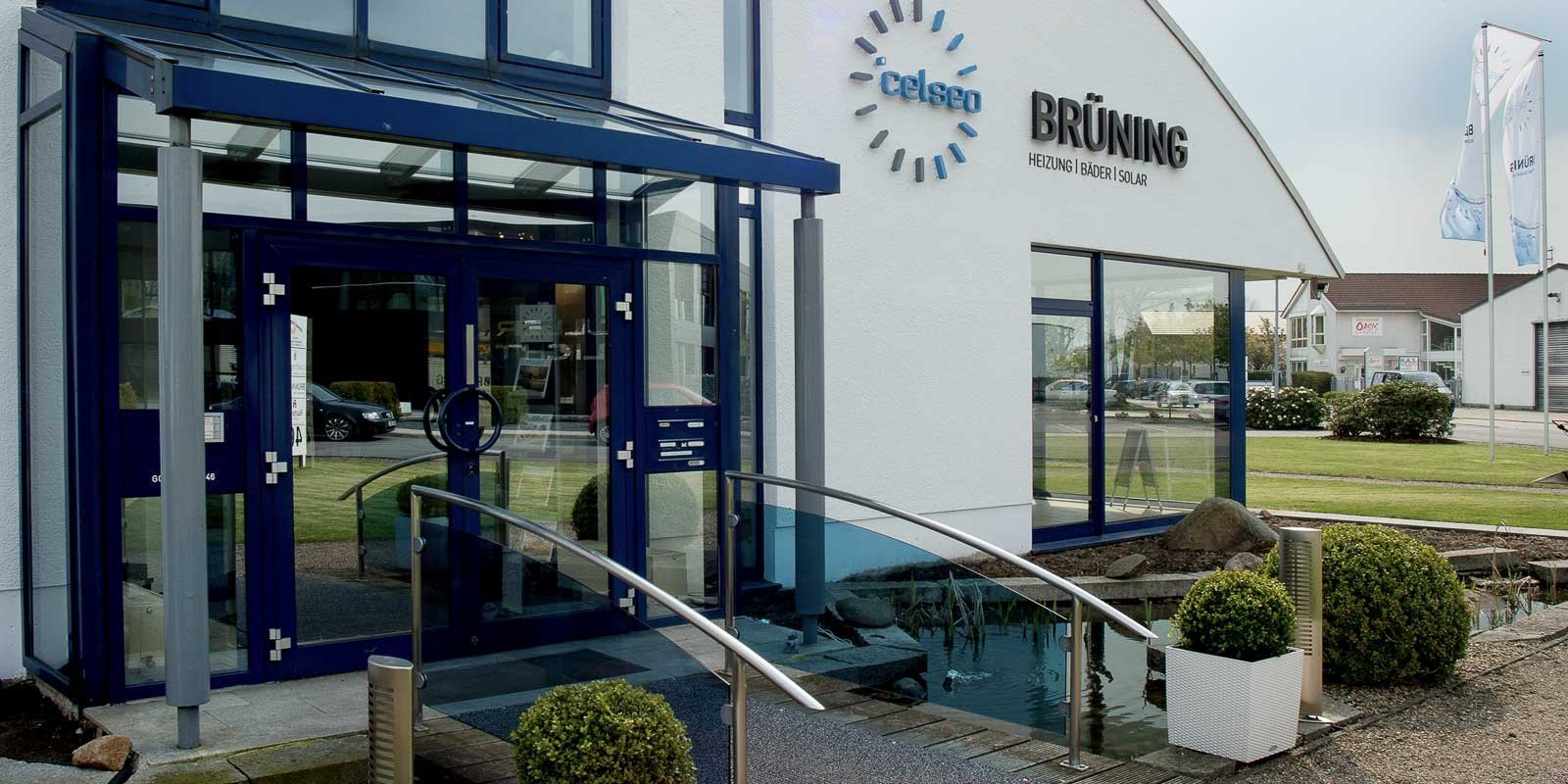 Das Gebäude hat eine klare, moderne Architektur mit einem auffälligen Logo und einem transparenten Vordach über dem Eingang.