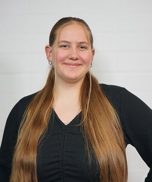 Eine junge Frau mit langen, glatten Haaren lächelt freundlich in die Kamera, während sie in einem schwarzen Oberteil posiert.