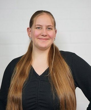 Eine junge Frau mit langen, glatten Haaren lächelt freundlich in die Kamera, während sie in einem schwarzen Oberteil posiert.