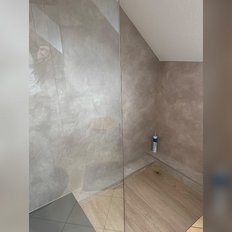 Der Duschbereich ist modern und schlicht, mit einem Holzfußboden und einer dekorativen Wandverkleidung in neutralen Farben.