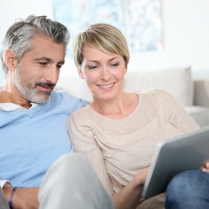 Ein Paaerchen sitzen nebeneinander und schauen auf ein Tablet