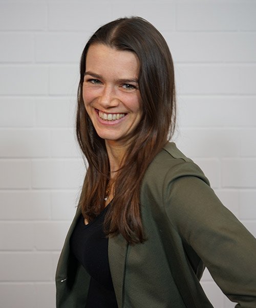 Die Frau zeigt ein fröhliches Lächeln und hat eine entspannte Haltung, während sie in einem modernen, hellen Raum steht.